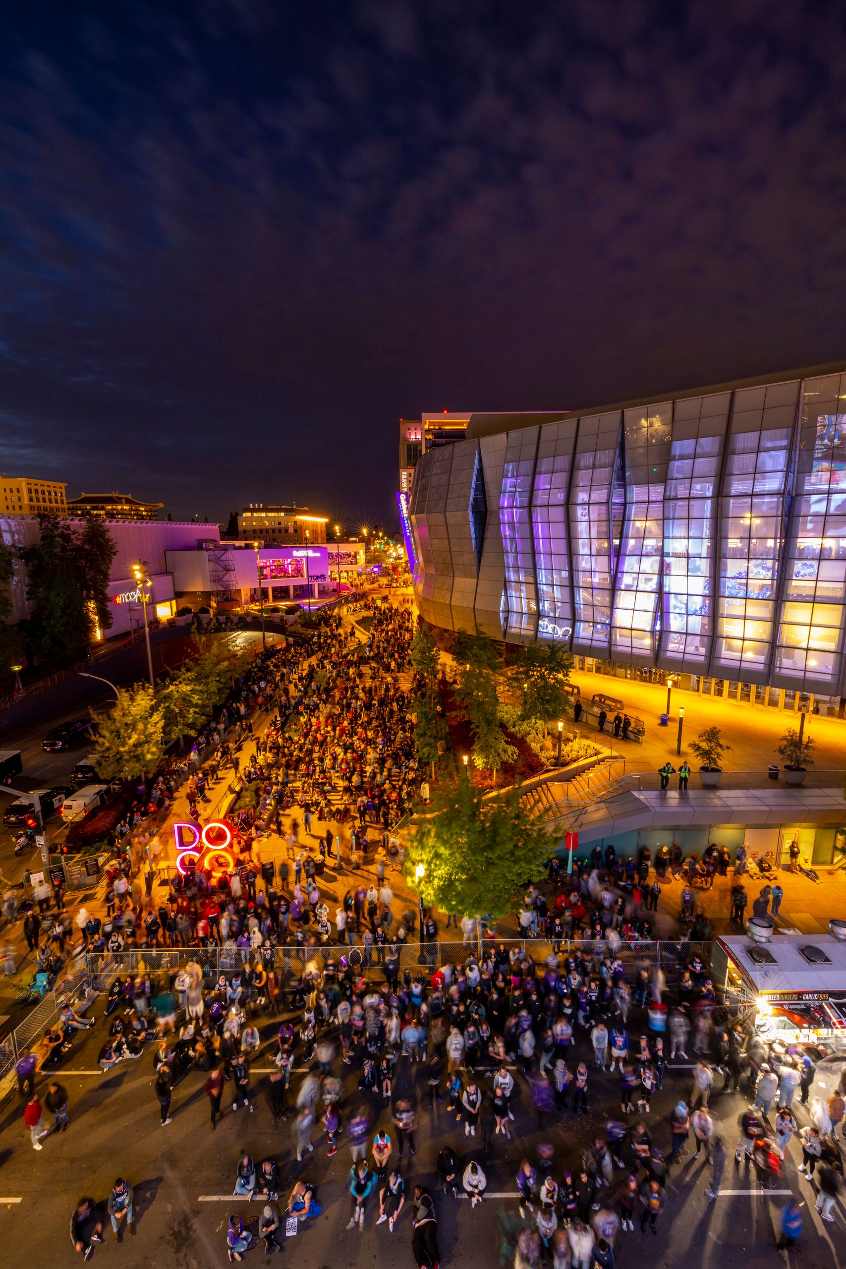 Vibrant night street festival with crowd and illuminated modern architecture.