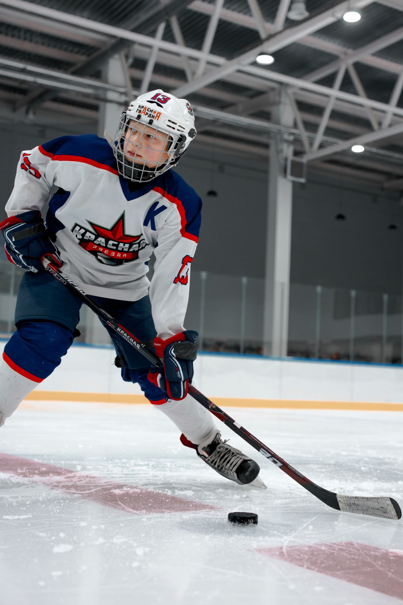 Young hockey player in full gear skates with intensity on ice rink.