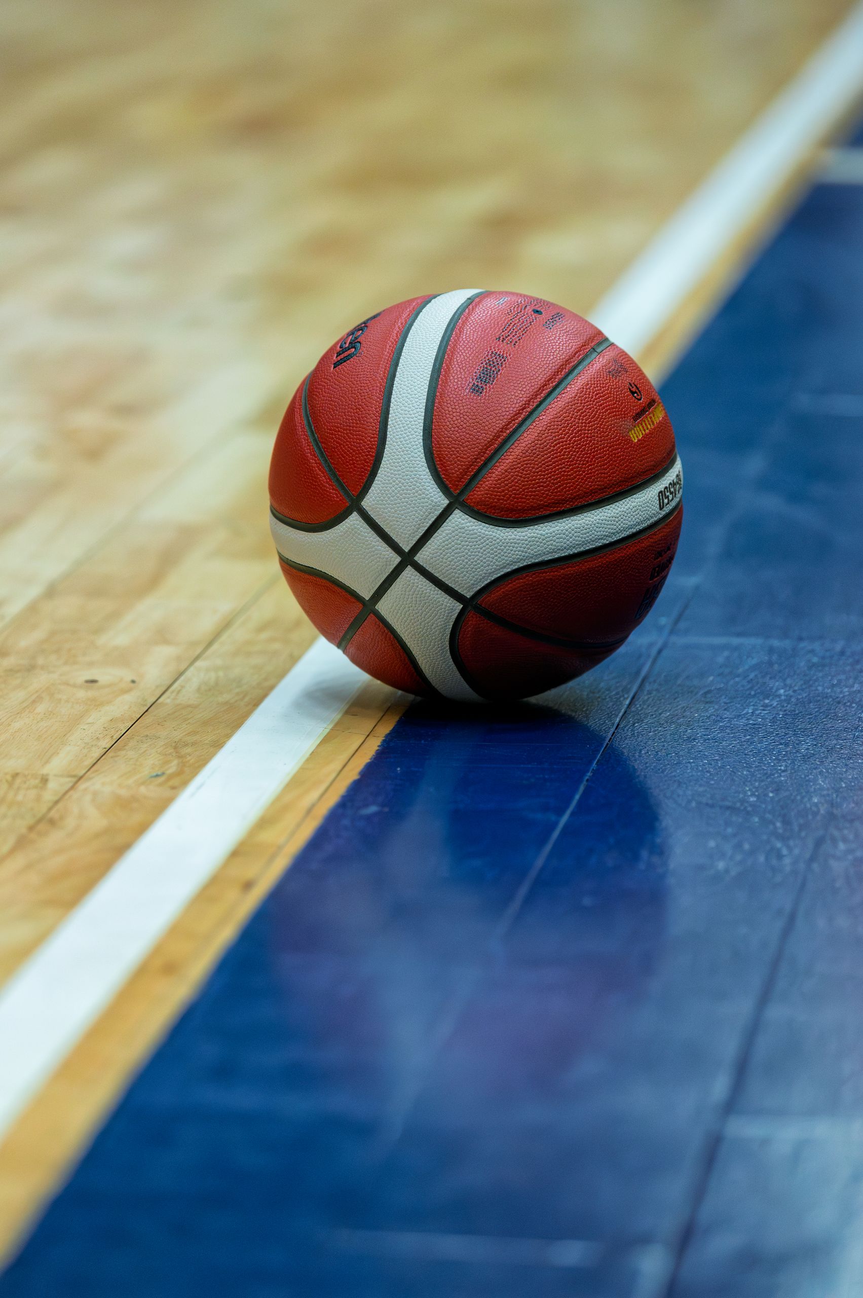 A basketball resting on the edge of a hardwood court with contrasting colors, creating a dynamic sports scene.