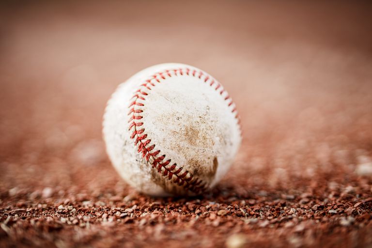 A close-up shot of a worn baseball resting on a gravel field, highlighting its texture and details.