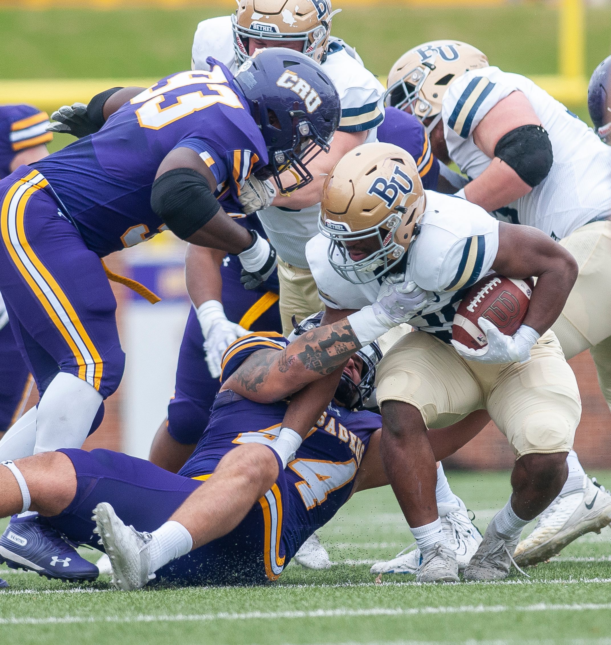 A dynamic moment in a college football game with players tackling on the field.