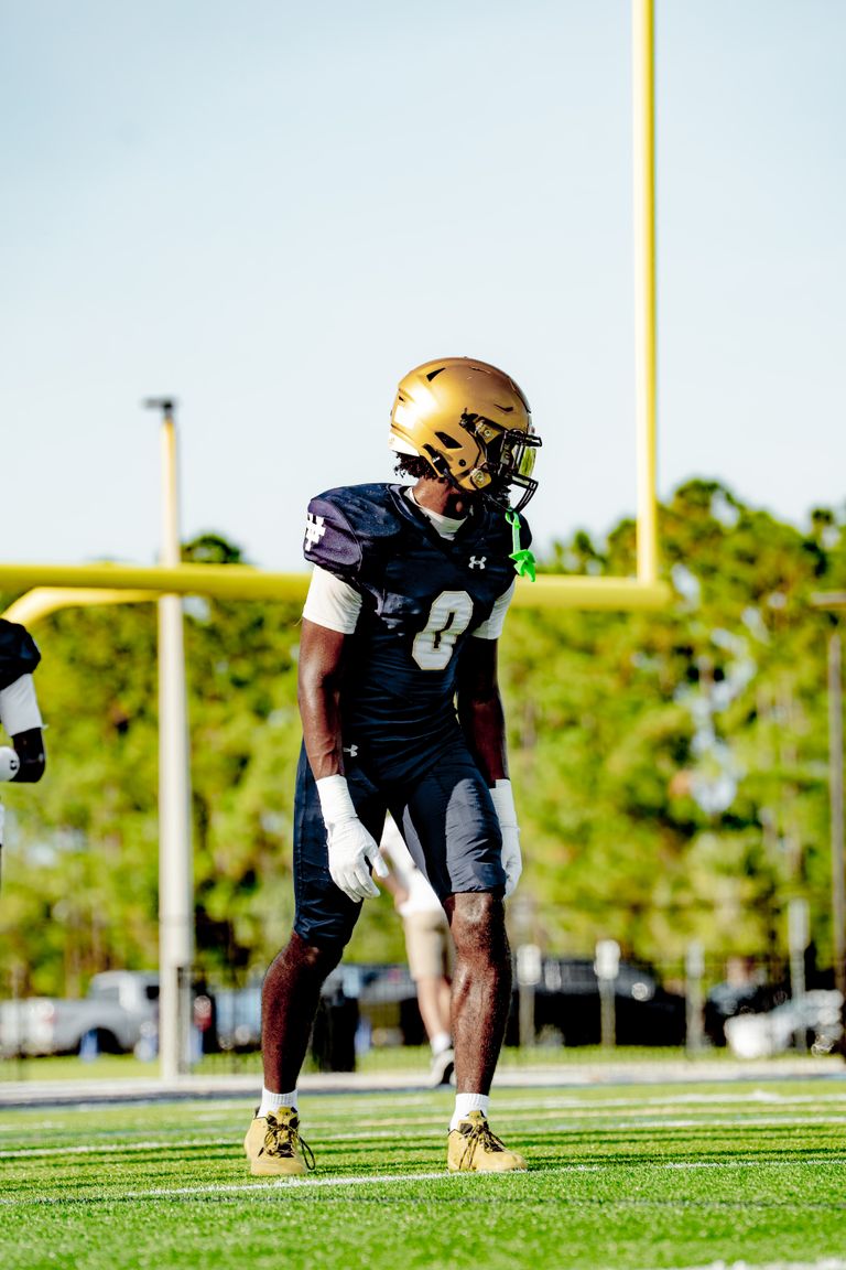 A football player in a black and gold uniform focuses during a game on a sunny day.