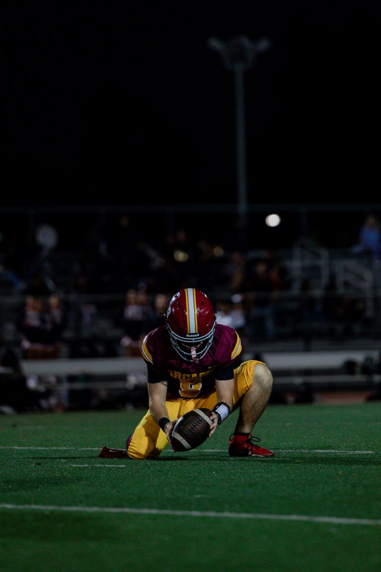 A football player prepares to hold the football steady for a placekick during a night game.