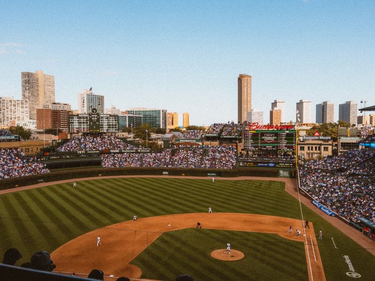 Aerial view of a lively baseball game at a famous stadium with city skyline.