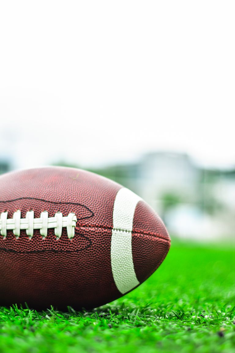 Detailed image of an American football resting on a green field, perfect for sports-themed content.