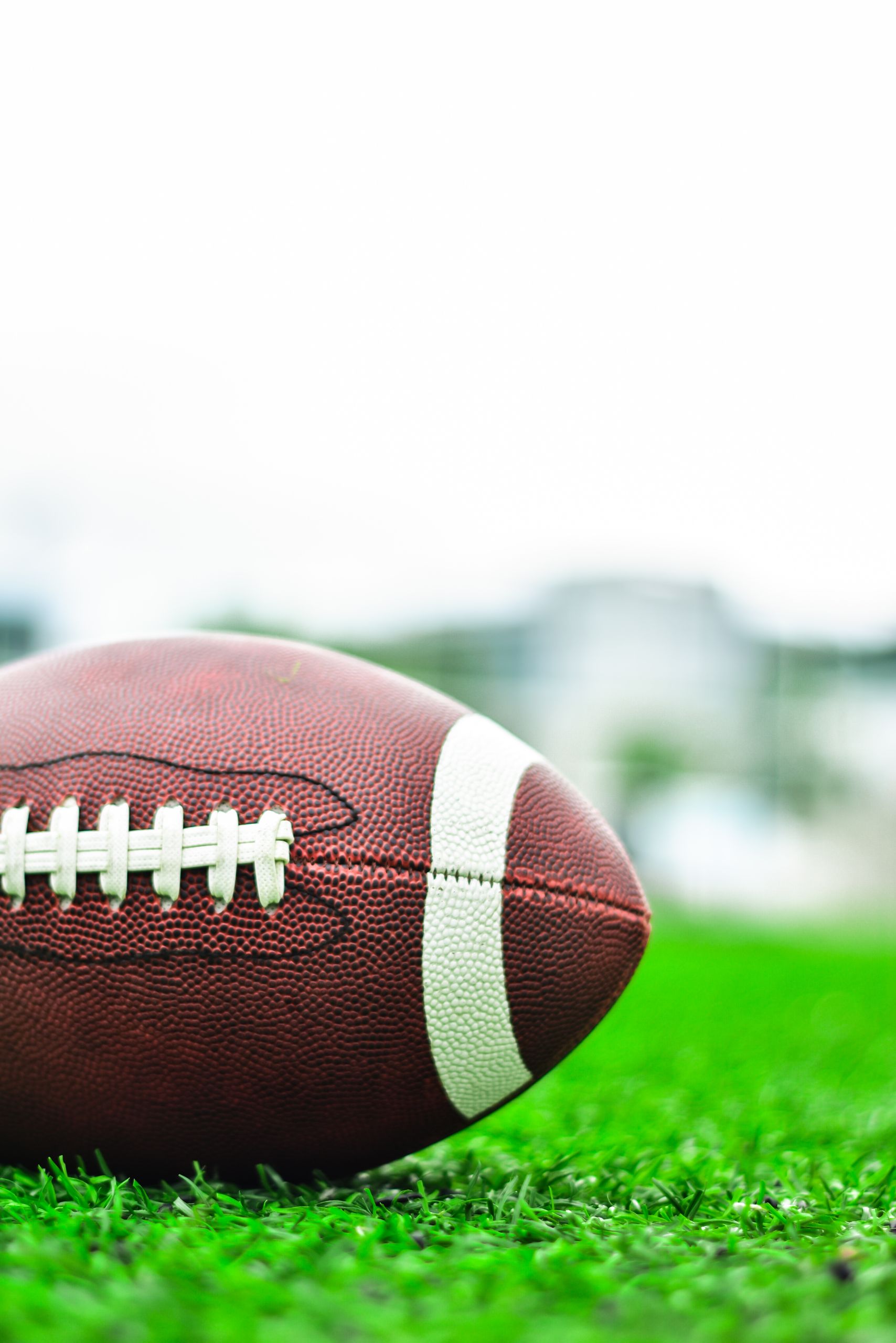 Detailed image of an American football resting on a green field, perfect for sports-themed content.
