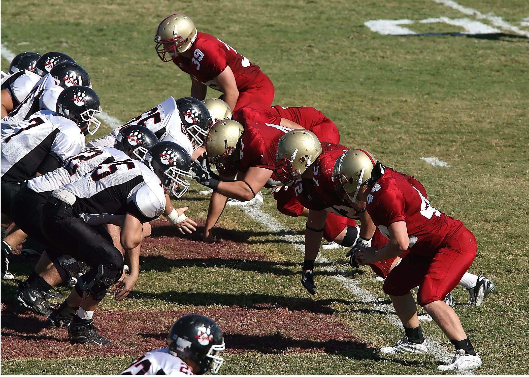 Intense moment as two American football teams face off at the line of scrimmage on a sunny day.