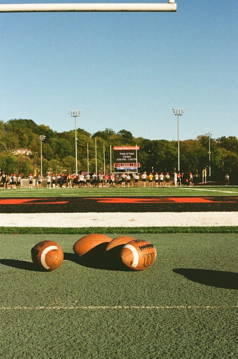 Three footballs on a green field with players in background