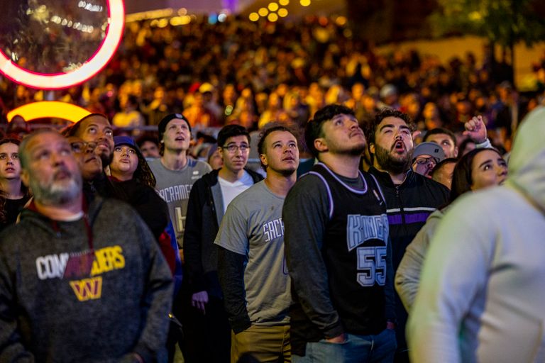 A diverse crowd gathers at night, watching a sports event with rapt attention.