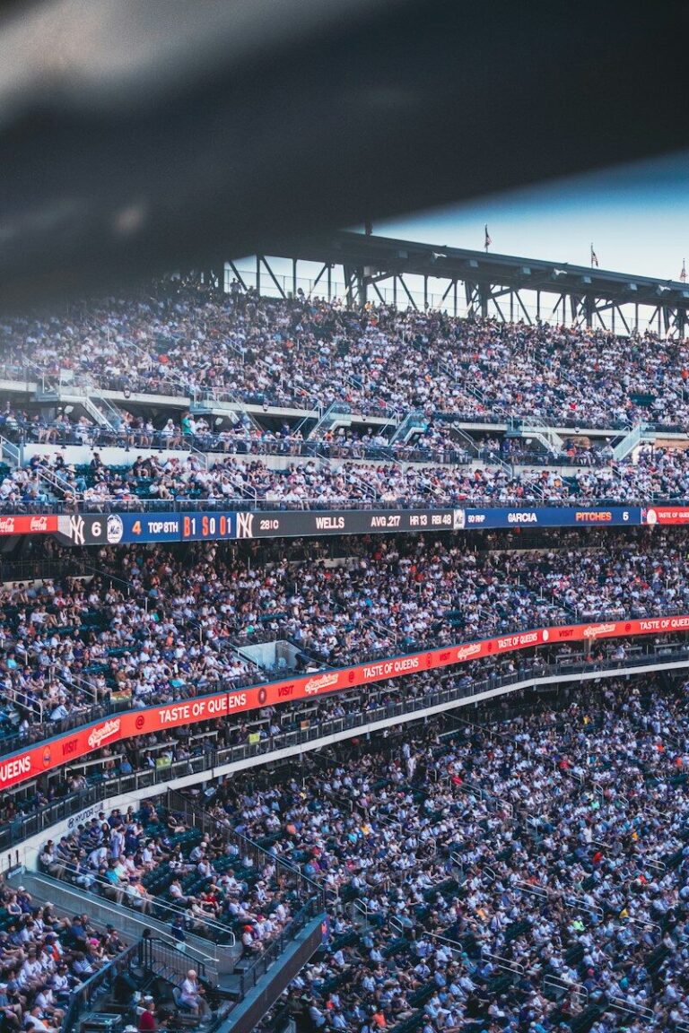 A crowded baseball stadium with spectators in the stands and a digital scoreboard displaying game statistics