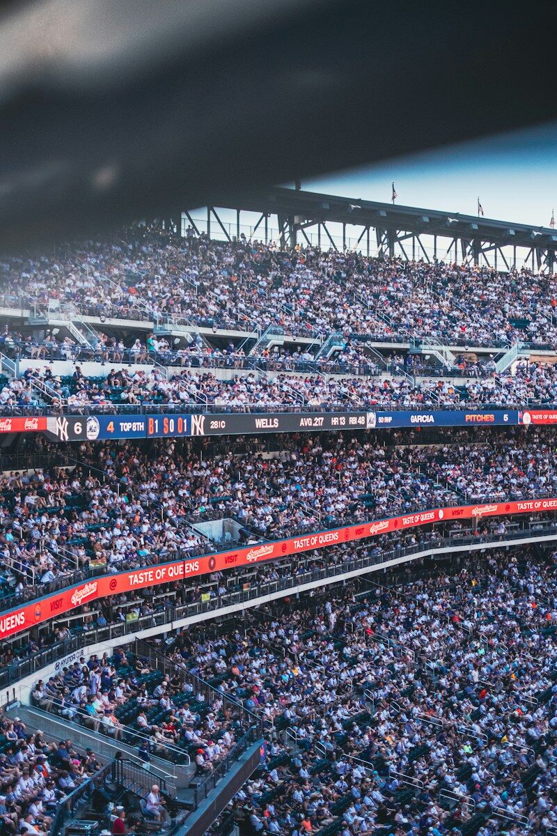 A crowded baseball stadium with spectators in the stands and a digital scoreboard displaying game statistics
