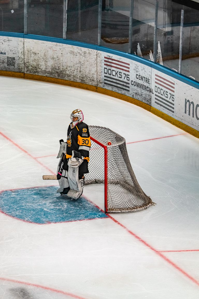 Ice hockey goalie stands ready at the net during a game in a professional indoor rink.