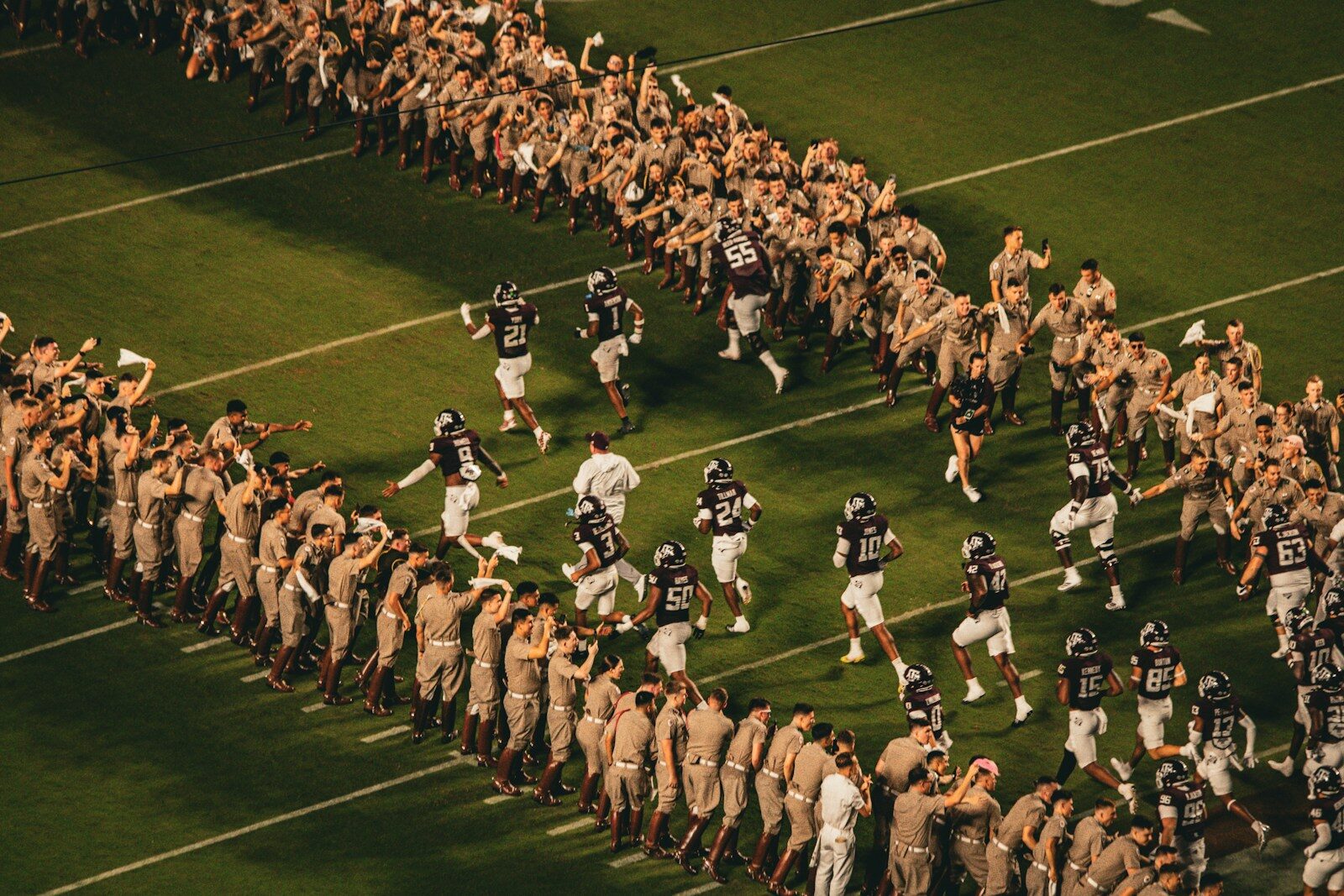 Football players run onto the field between cheering crowds