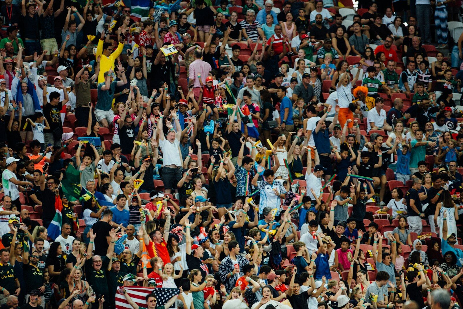 A crowd of people in a stadium cheering with arms raised in celebration